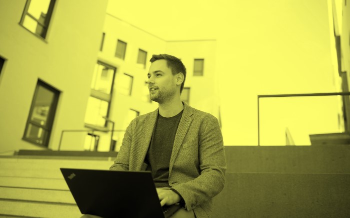 Mann mit Laptop sitzt auf Mauer